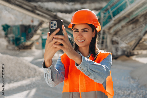 Fotografie Smiling beautiful woman wearing safety hard hat and orange vest taking photo, ho