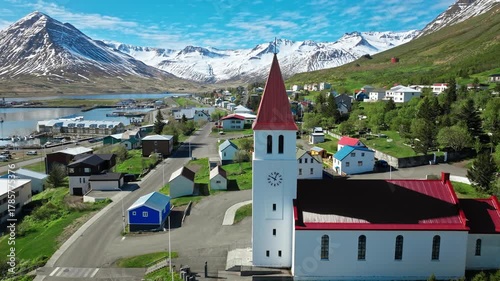 Drone shot of the iconic white and red-roofed church in Siglufjordur, North Iceland, under clear blue skies.