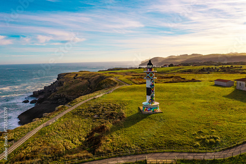 Fotografija Colorful Ajo Lighthouse captured by drone, standing on a green cliff with a vast ocean backdrop