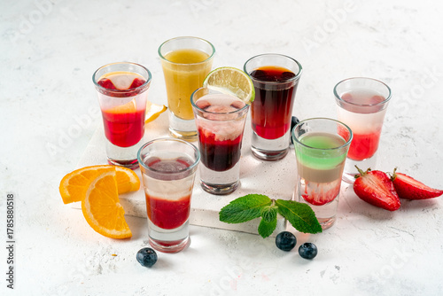 Various alcoholic drinks in glasses on a white table, mixed shots of berries and oranges