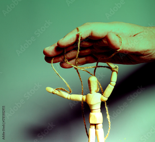 Man's hand pulling strings of wooden puppet on gray background. Concept of emotional manipulation,dictatorship and control