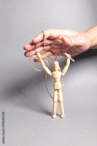 Man's hand pulling strings of wooden puppet on gray background. Concept of emotional manipulation,dictatorship and control