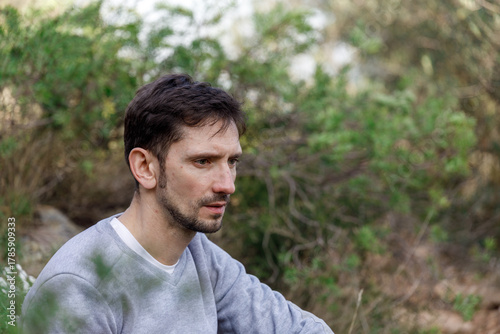 Man with a beard and a grey shirt is sitting in a forest