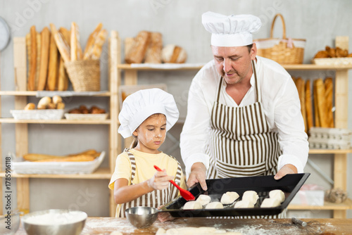 Valokuva Daughter helps father baker to make pastries, lubricate croissants with loosened
