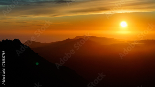 Aerial view of the sun blazing intensely over the shadowy silhouettes of mountains, as if the world is on fire, Cape Town, Western Cape, South Africa.