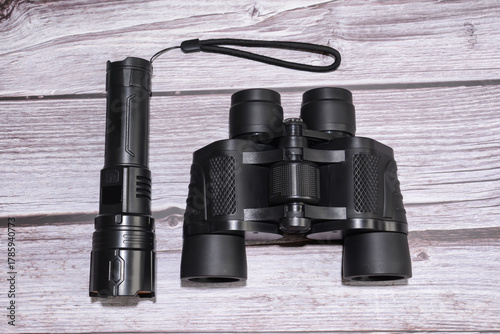 Binoculars and a flashlight on a wooden table. Black binoculars, black flashlight.