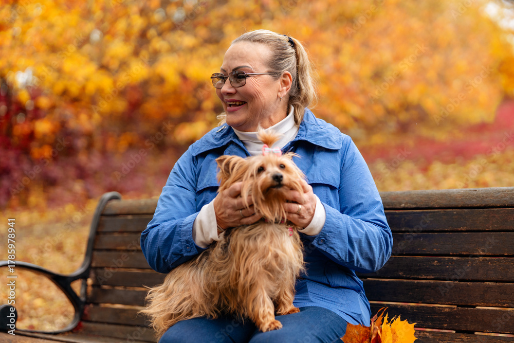 Naklejka premium Smiling woman enjoys time with small dog in colorful autumn park