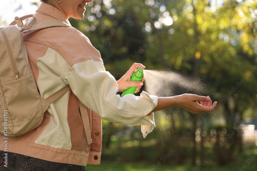 Αυτοκόλλητο Woman spraying tick repellent onto hand in park, closeup