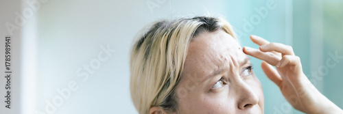 Bild auf Leinwand Unhappy middle-aged Caucasian businesswoman feeling worried, concerned about signs of aging like wrinkles and acne on her facial skin