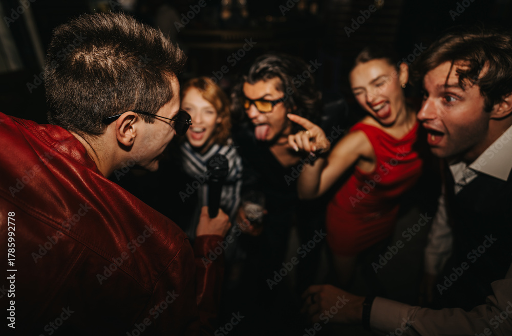 Fototapeta premium A lively night out with friends enjoying music, singing into a microphone, and dancing in a dark venue. Their energy and smiles capture celebration, togetherness, and social fun.