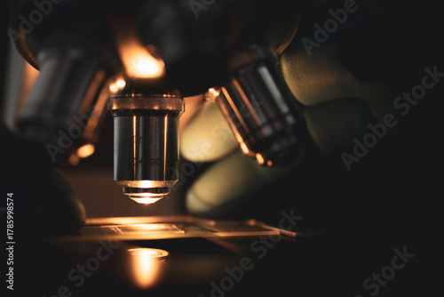 High-quality close-up image of a laboratory microscope being adjusted by a scientist in gloves. Represents science precision, healthcare innovation, and biotechnology research.