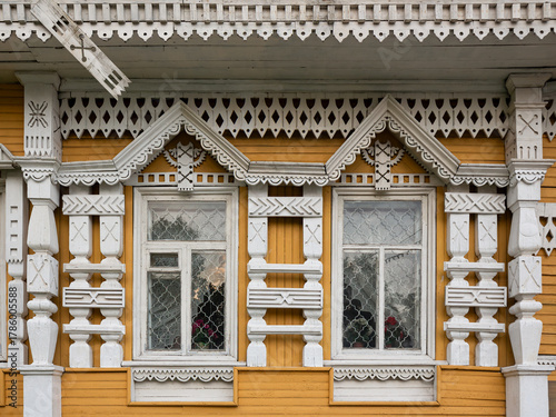 Beautiful cornices and window with carved trims. The yellow wall of a wooden house is decorated with white lace decorative elements. Russian wooden architecture. Uglich, Yaroslavl Region, Russia.