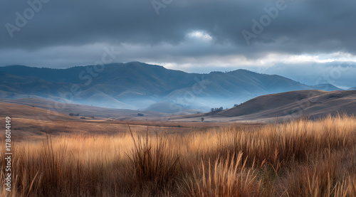 Grassy hills rise under a moody sky, creating a peaceful landscape at twilight in a mountain area