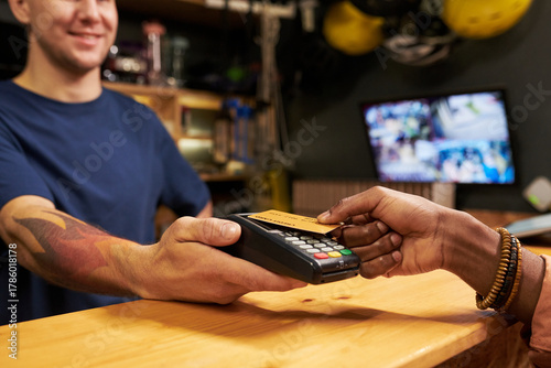 Young man holding payment terminal while Black young woman making contactless payment with credit card at counter