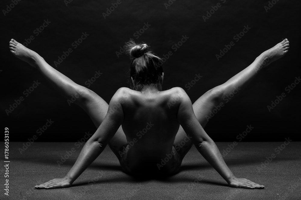 Naklejka premium Attractive adult woman twisting fit body and meditates in a yoga pose on black background. Female with slim, strength and flexibility body.