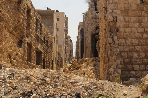 Φωτογραφία War damaged street in Aleppo, Syria, with destroyed stone buildings and rubble blocking the way