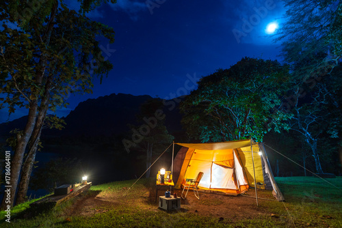 Night camping adventure with a cozy tent lit under the starry sky in a summer forest