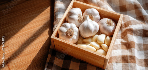 Fresh garlic cloves and bulbs are arranged in wooden box on checkered cloth, showcasing their natural beauty and health benefits. Garlic is staple food known for its flavor and health properties