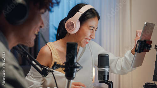 Close-up Young happy Asia couple wear headphone sit on desk online live streaming football live score watch soccer sport game on laptop use microphone talk with follower small studio in home at night.