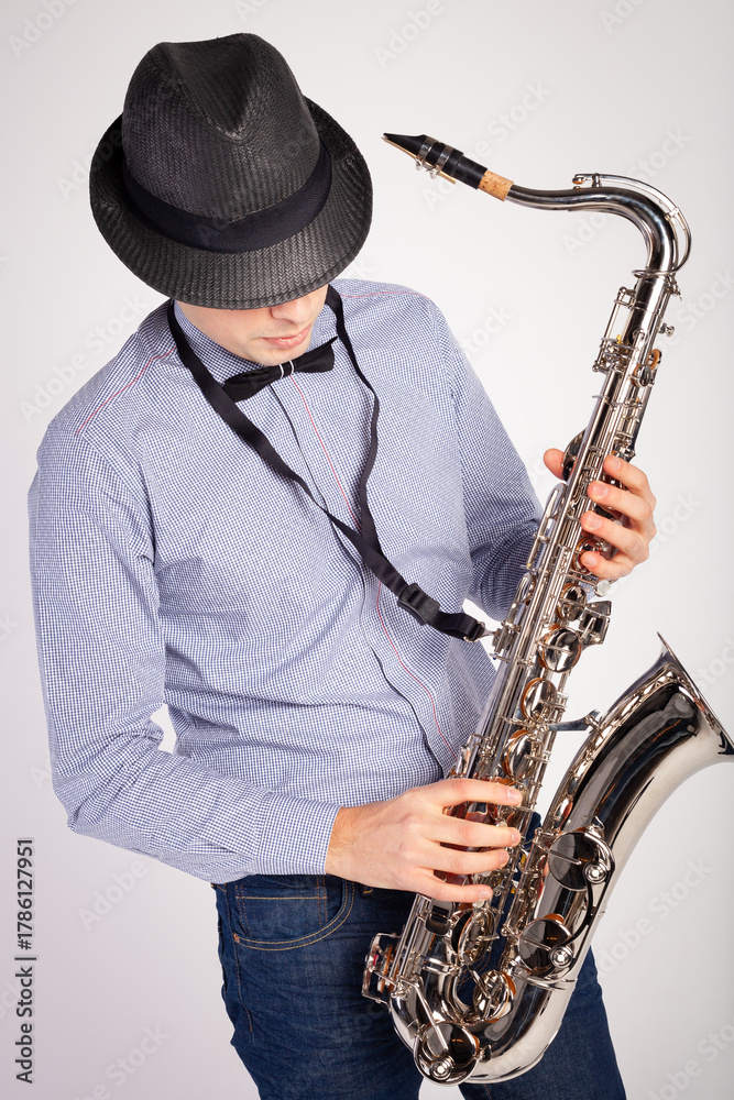 Fototapeta premium Portrait of stylish man in hat playing saxophone, performing isolated over white background. Jazz performer