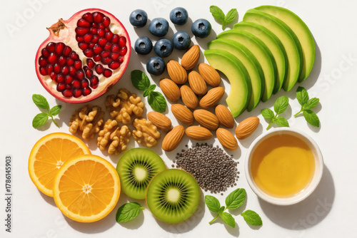 A vibrant assortment of healthy foods, including pomegranate, avocado, kiwi, almonds, walnuts, blueberries, orange slices, chia seeds, and honey