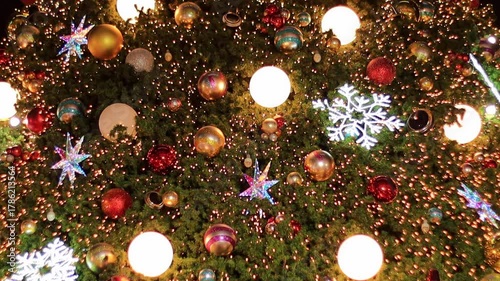 A detailed shot of a large, beautifully decorated Christmas tree. Features sparkling lights, shiny metallic balls, red and gold ornaments, and star shaped decorations. Perfect for holiday 