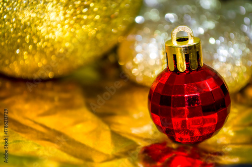 A shiny red Christmas ornament stands alone on a golden surface, surrounded by sparkling gold and silver decorations, creating a festive holiday atmosphere. Copy space. 