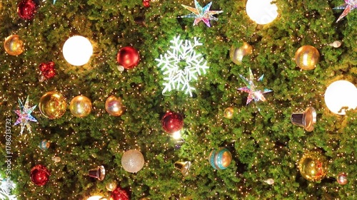 A detailed shot of a large, beautifully decorated Christmas tree. Features sparkling lights, shiny metallic balls, red and gold ornaments, and star shaped decorations. Perfect for holiday 