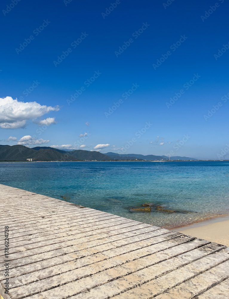 Fototapeta premium Mountain and ocean views from a wooden pier under a clear blue sky