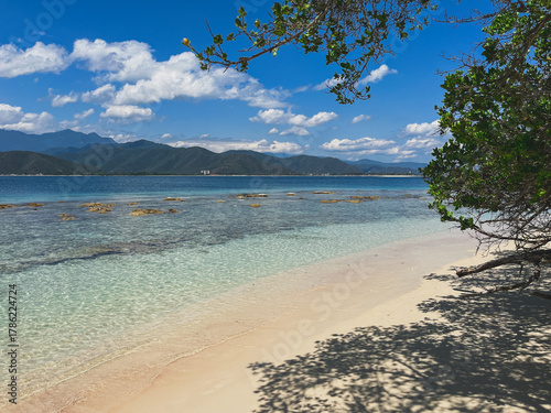Idyllic tropical beach landscape with crystal clear waters, white sand and mountain views