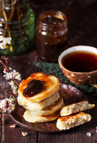 Lenten yeast pancakes with plum jam and tea, and a bouquet of blooming apricot branches on a wooden table.