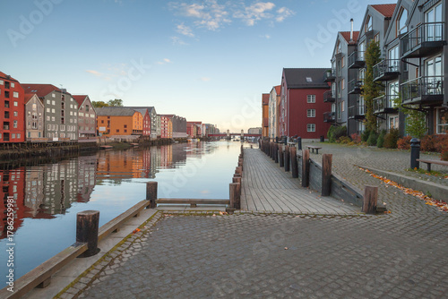 Vibrant rows of colorful houses line a tranquil canal, with a stone promenade