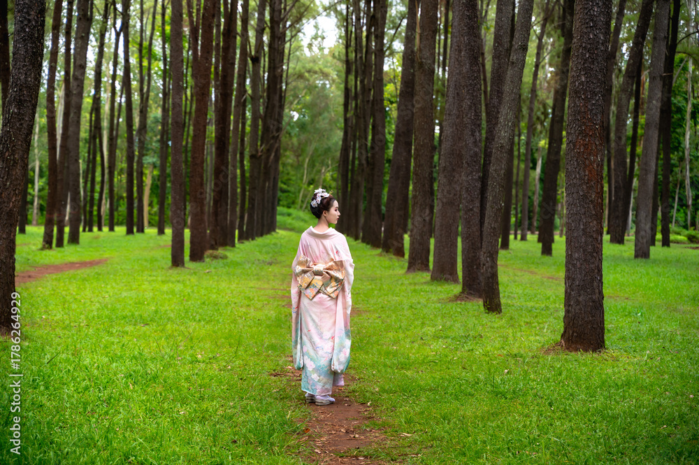 Fototapeta premium Young pretty Japanese woman in elegant traditional kimono or yukata walking in garden