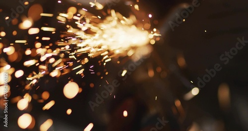 Streaming orange-yellow sparks across dark bench making embers, bokeh, smoke, source off-frame