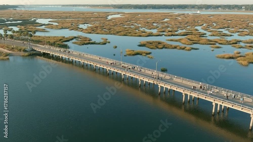 Aerial view of people doing a volksmarch or running race over a bridge surrounded by water.