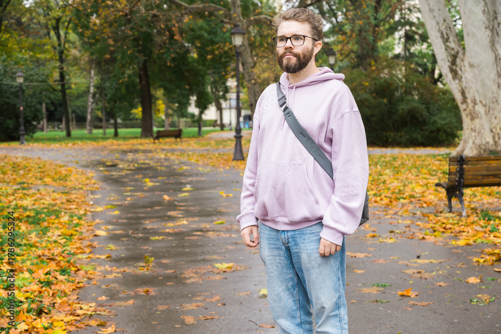Obraz premium Man standing on path covered with leaves in city park. Copy space and empty place for advertising. Autumn atmosphere, awareness, and daily reflection.
