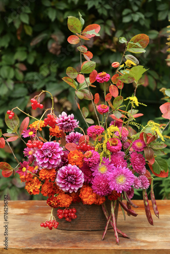 Beautiful autumn bouquet with dahlia, aster, marigold flower and colorful leaves on table in garden. Fall pink yellow orange red purple flowers close up