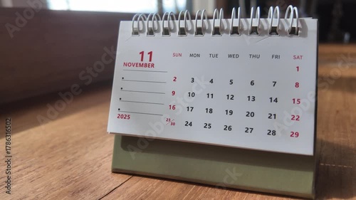 Slow motion footage of November 2025 calendar page on a wooden table. 4K Horizontal