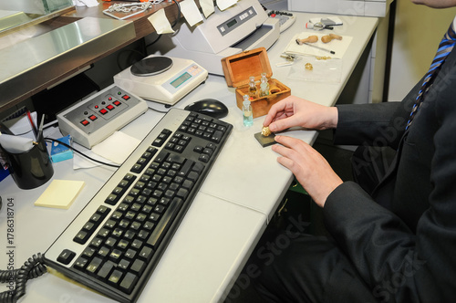 Принти на полотні A man in a suit checks the purity of a gold jewel on a touchstone