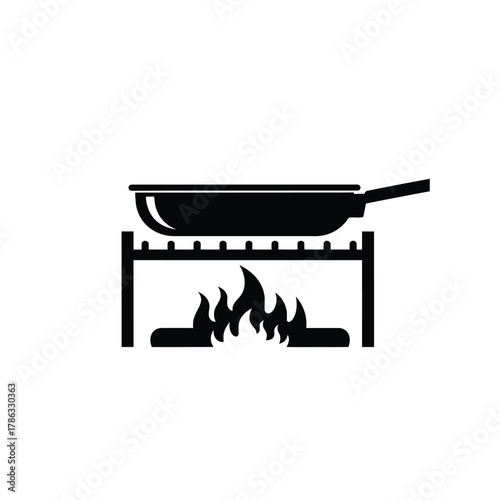 Black frying pan cooking over open flames on a grill