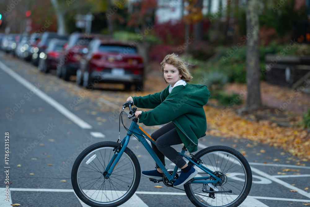 Obraz premium Fall city scene with child on bike. Kid rides bike in street. Child joyful ride bike in the city street. Child rides bike on autumn. Happy child learning to ride.