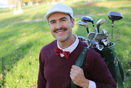Фотография Handsome vintage golf caddie carrying clubs on golf course.