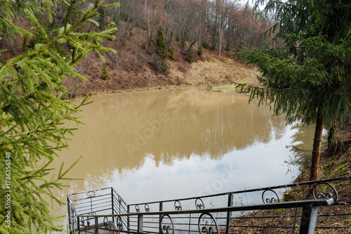 Fotografie Erosion marks on old fence, Concrete steps lead to muddy waters, Mosscovered rai