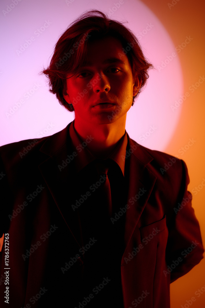 Fototapeta premium Stylish young man poses confidently against a vibrant backdrop of colors and light