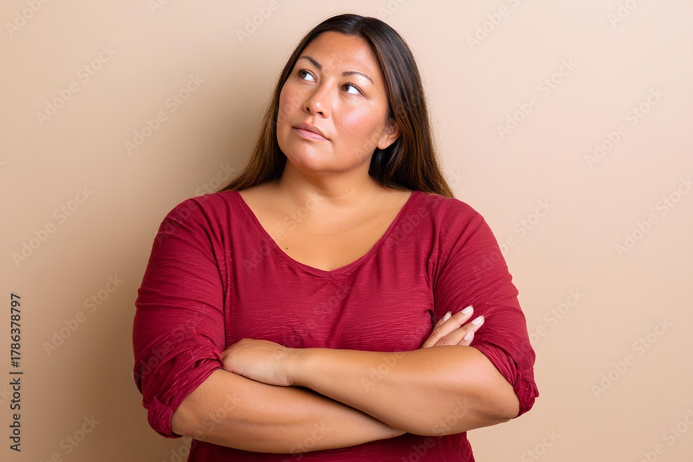 Obraz premium Confident plus size Latina woman with long hair, wearing a red shirt, poses thoughtfully against a neutral background, showcasing natural beauty and self-assurance