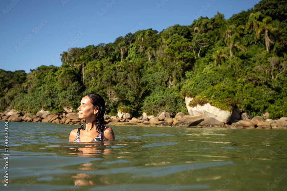 Fototapeta premium Woman enjoying a peaceful moment in the calm waters near a lush tropical coastline at midday