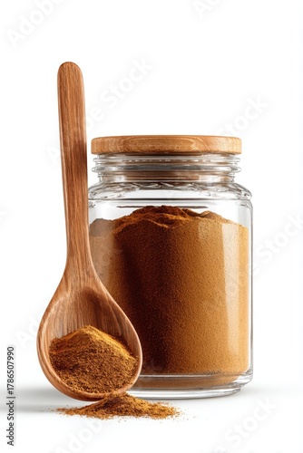 Glass jar of cinnamon powder with a wooden spoon full of the fragrant spice resting in front on a white background