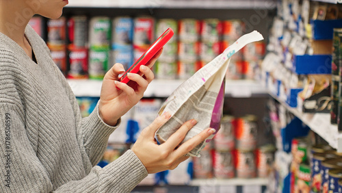 Woman scanning dry pet food using smartphone in pet store. Modern customer checking product information and ingredients using mobile app, AI assistant. Smart shopping Conscious choice Digital retail