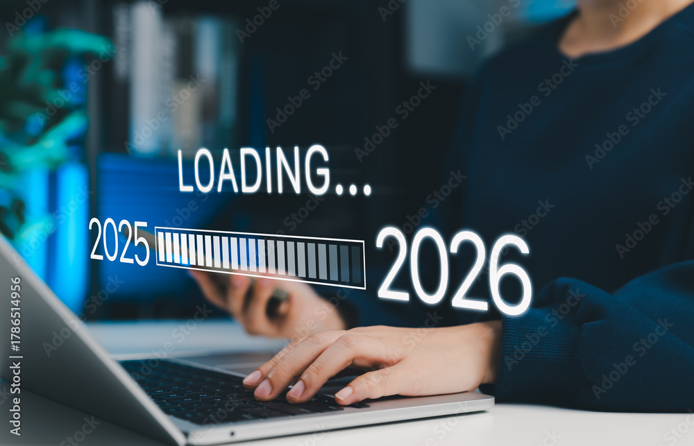 Fototapeta premium New year transition concept. Woman using laptop with progress bar loading from 2025 to 2026, symbolizing planning, change, goal setting, upcoming year, and digital transformation for future goals.