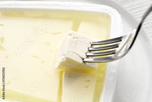 Картината върху платно Feta cheese in brine with fork in a plastic container